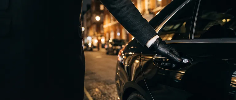 Chauffeur's gloved hand on the rear door of a luxury car