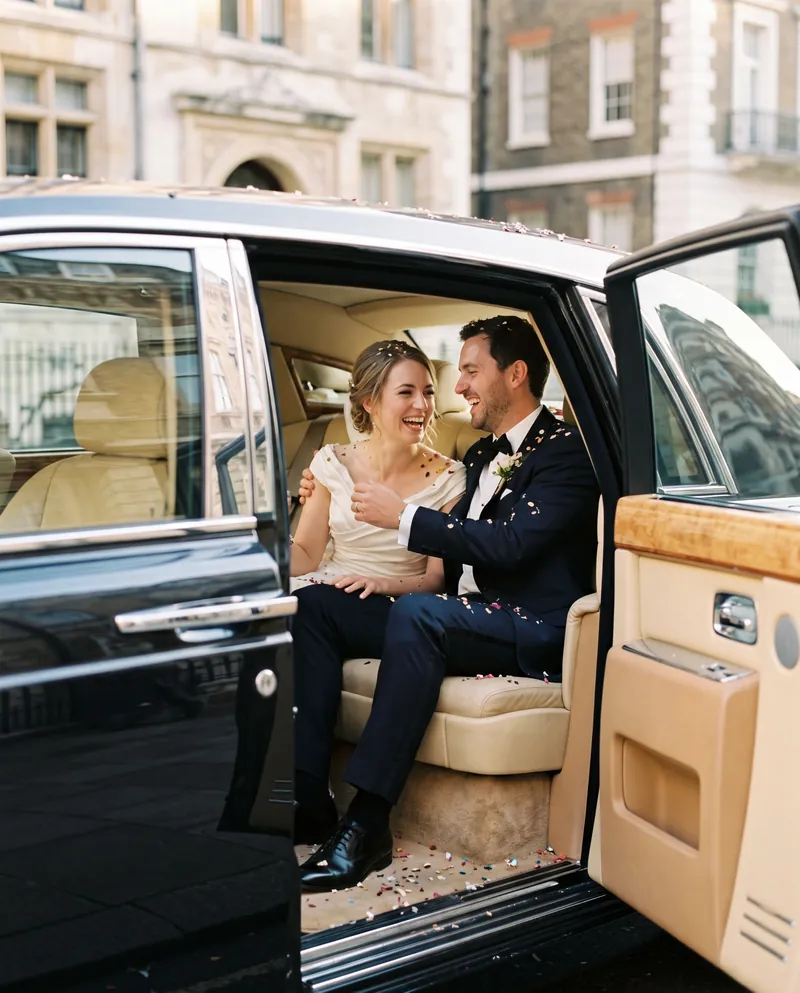 Newlyweds laughing in the rear of a Rolls-Royce